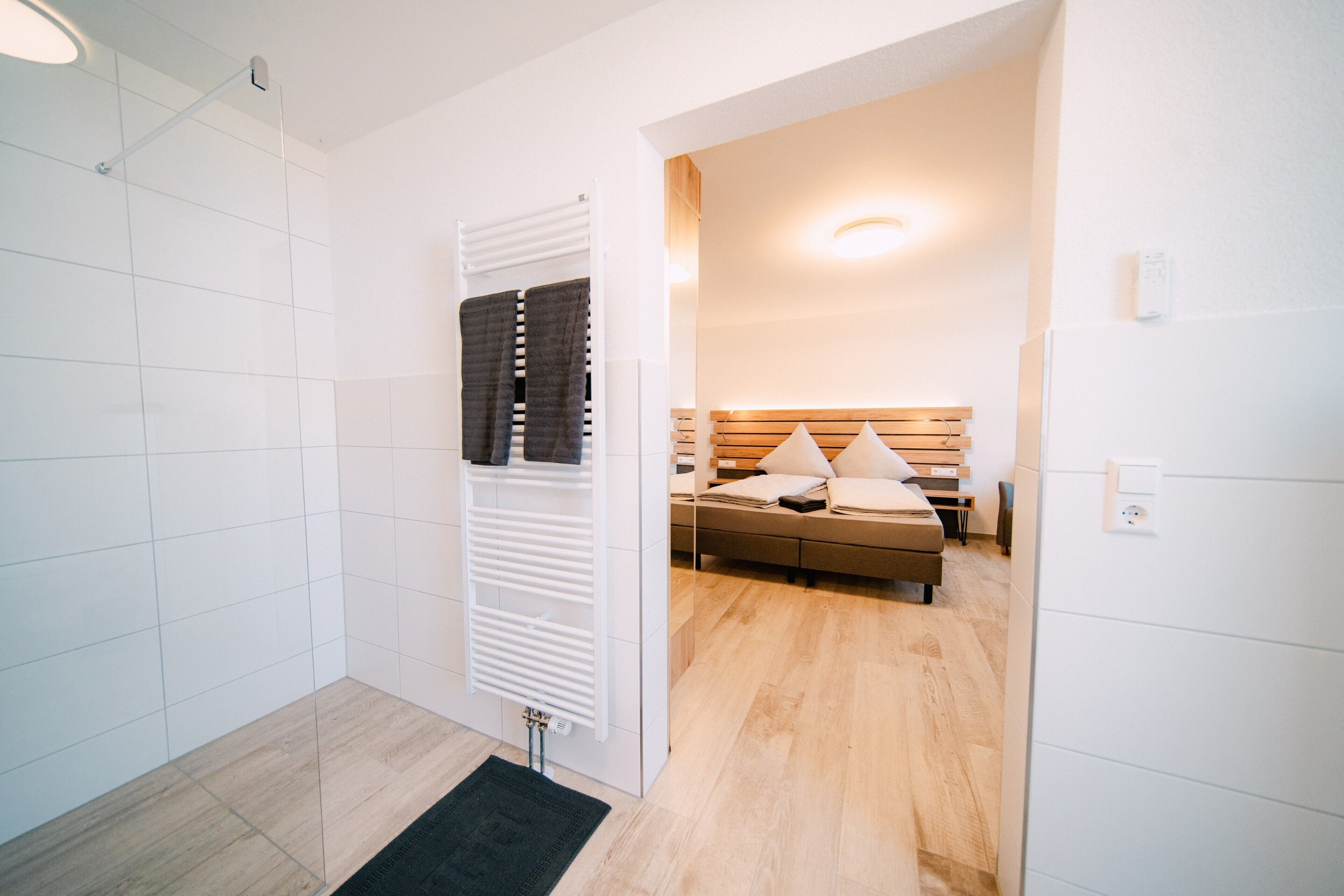 Une chambre d’hôtel avec un plancher en bois, un lit doté d’une tête de lit en bois, une table de chevet et un radiateur fixé au mur.