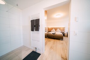 A hotel room with a wooden floor, a bed with a wooden headboard, a bedside table, and a wall-mounted radiator.