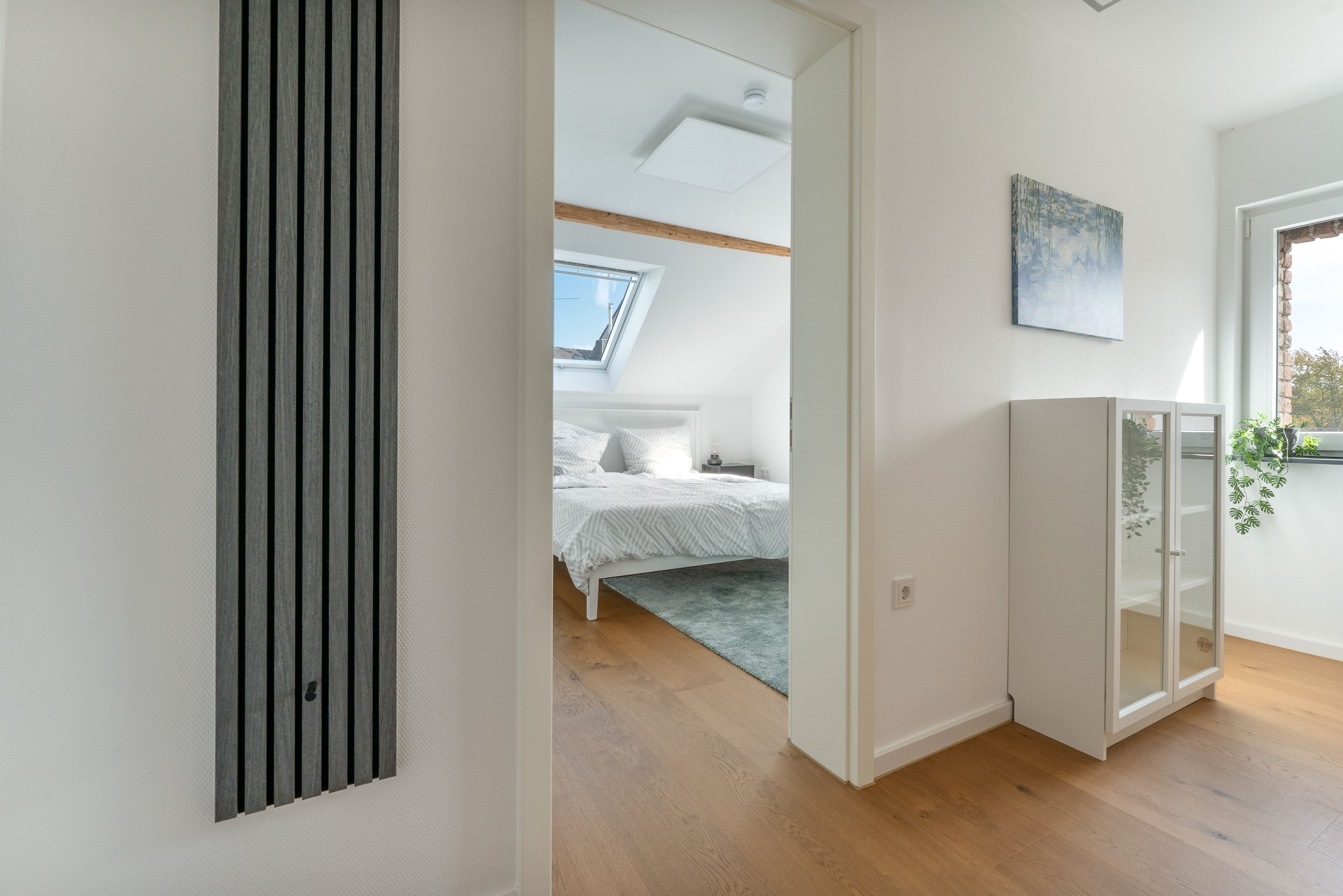 Ein Schlafzimmer mit Dachfenster, einem Bett mit weißer Bettwäsche, einem grauen Teppich und einem weißen Schrank mit Glastüren.