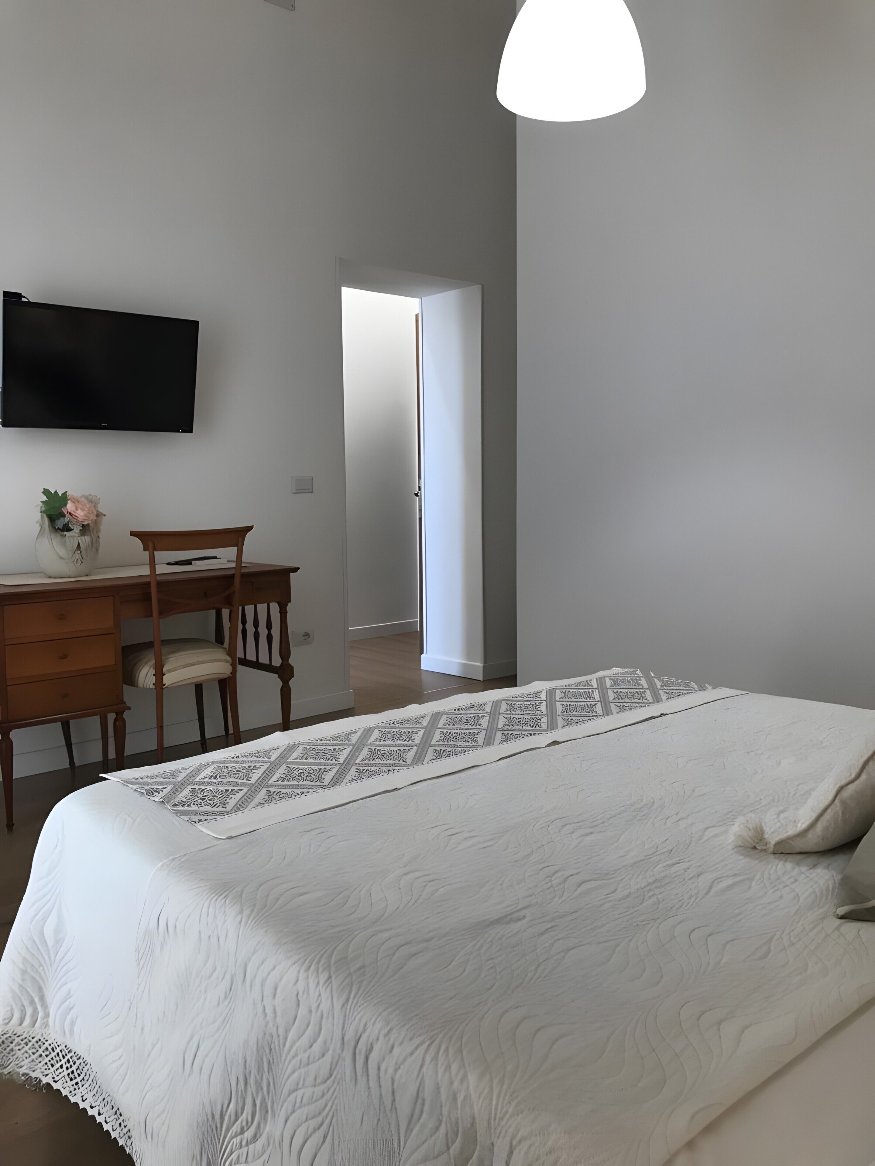Ein Schlafzimmer mit einem Bett, einem Schreibtisch, einem Stuhl, einem Fernseher und einer Tür zu einem anderen Raum.