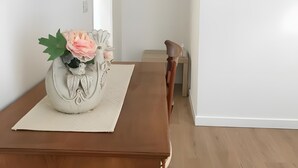 A dining area with a wooden table, a vase with flowers, and a television mounted on the wall.