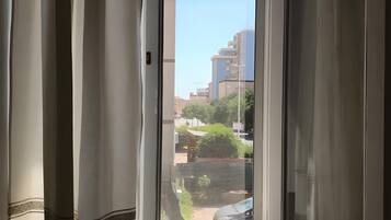A window with curtains partially drawn, revealing a view of buildings and greenery outside.
