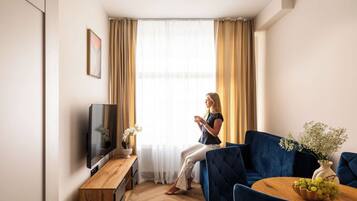 A modern living room with a sofa, a coffee table with a vase of flowers, a television, and a window with curtains.