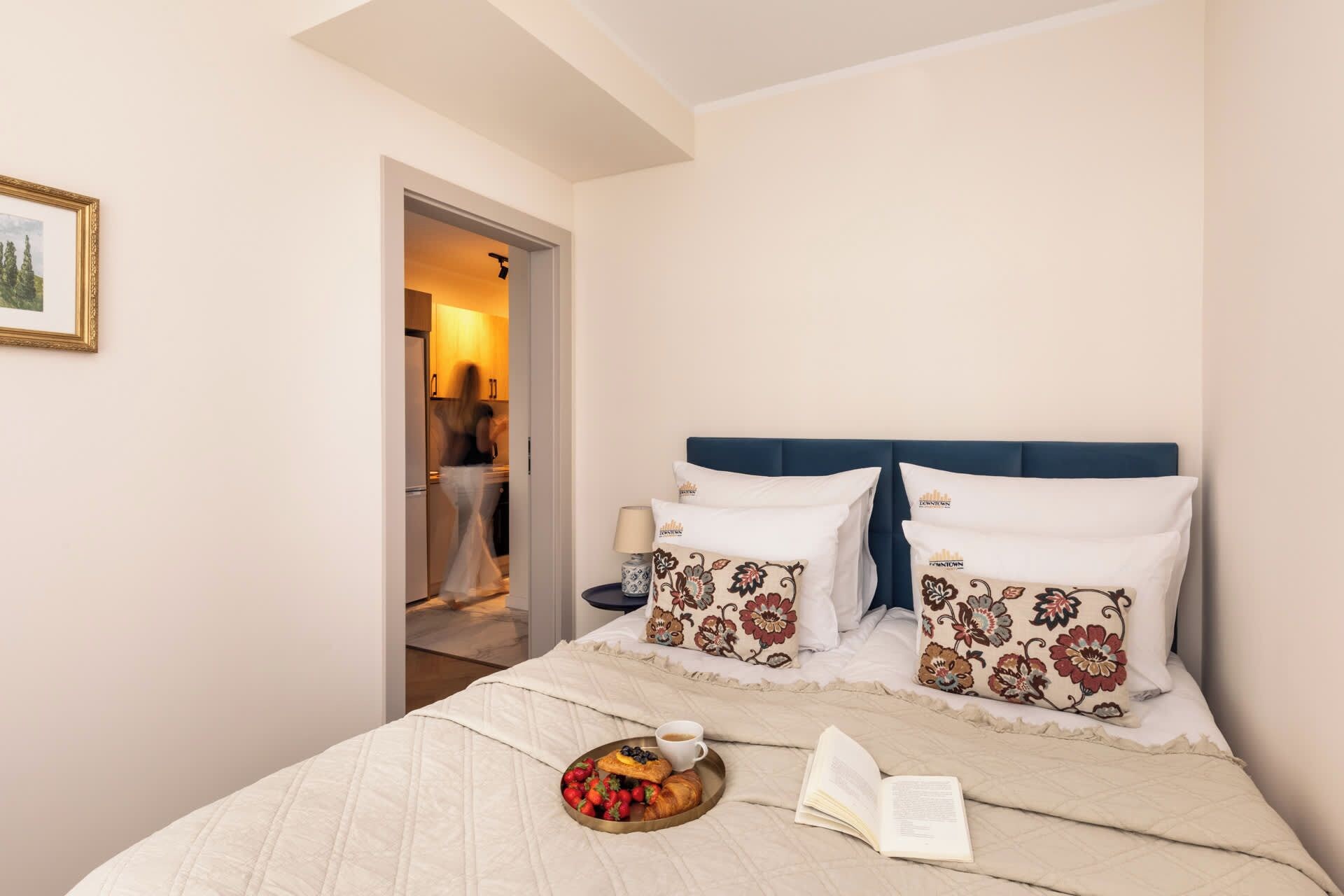 A bedroom with a bed, pillows, a tray with food and drink, and an open book.