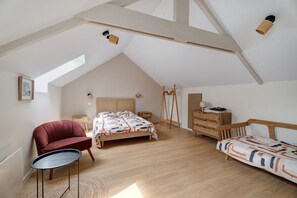 Un dormitorio con techo inclinado, una cama, una silla, un aparador y una mesita.