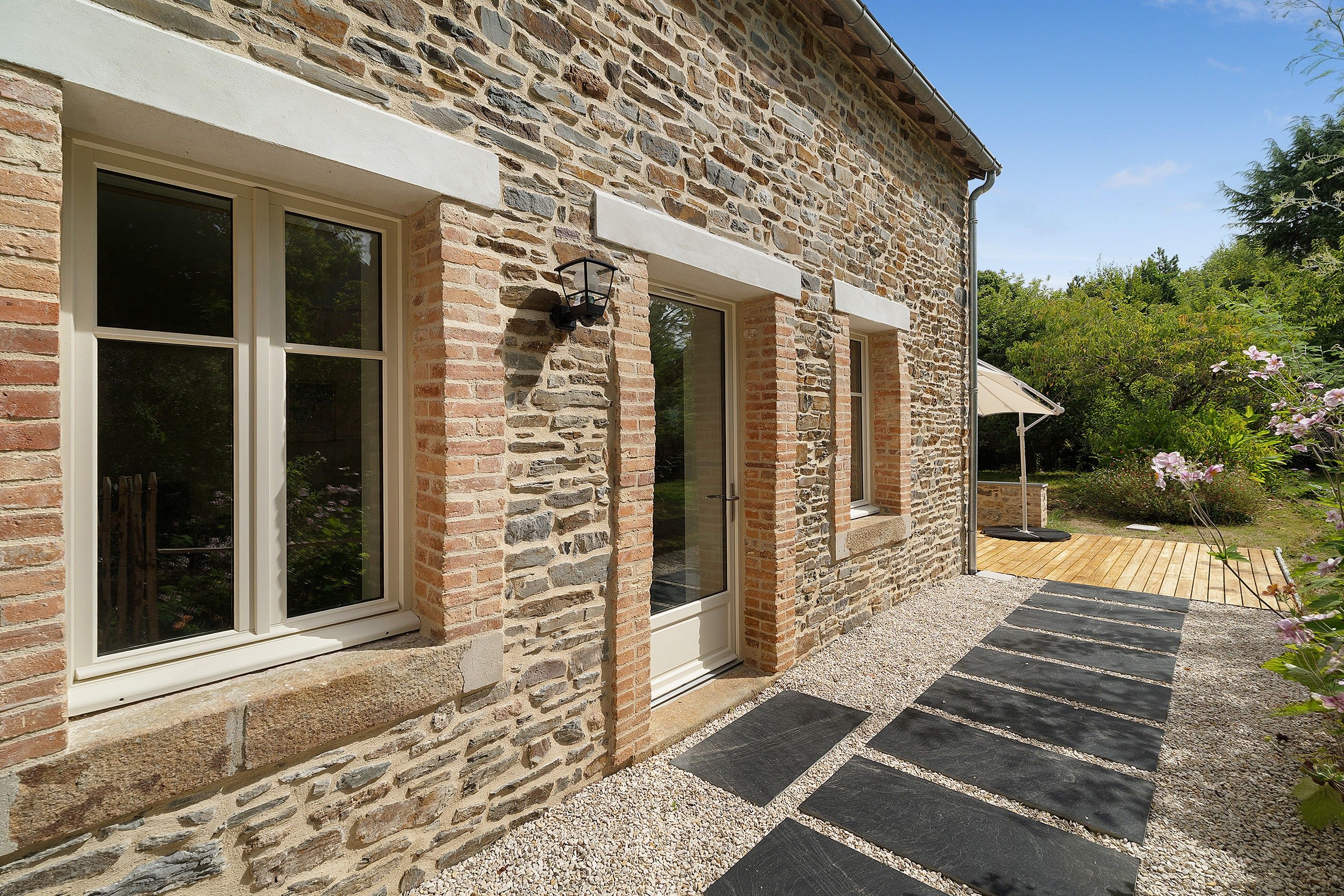 A stone building with large windows and a gravel pathway leading to a wooden deck.