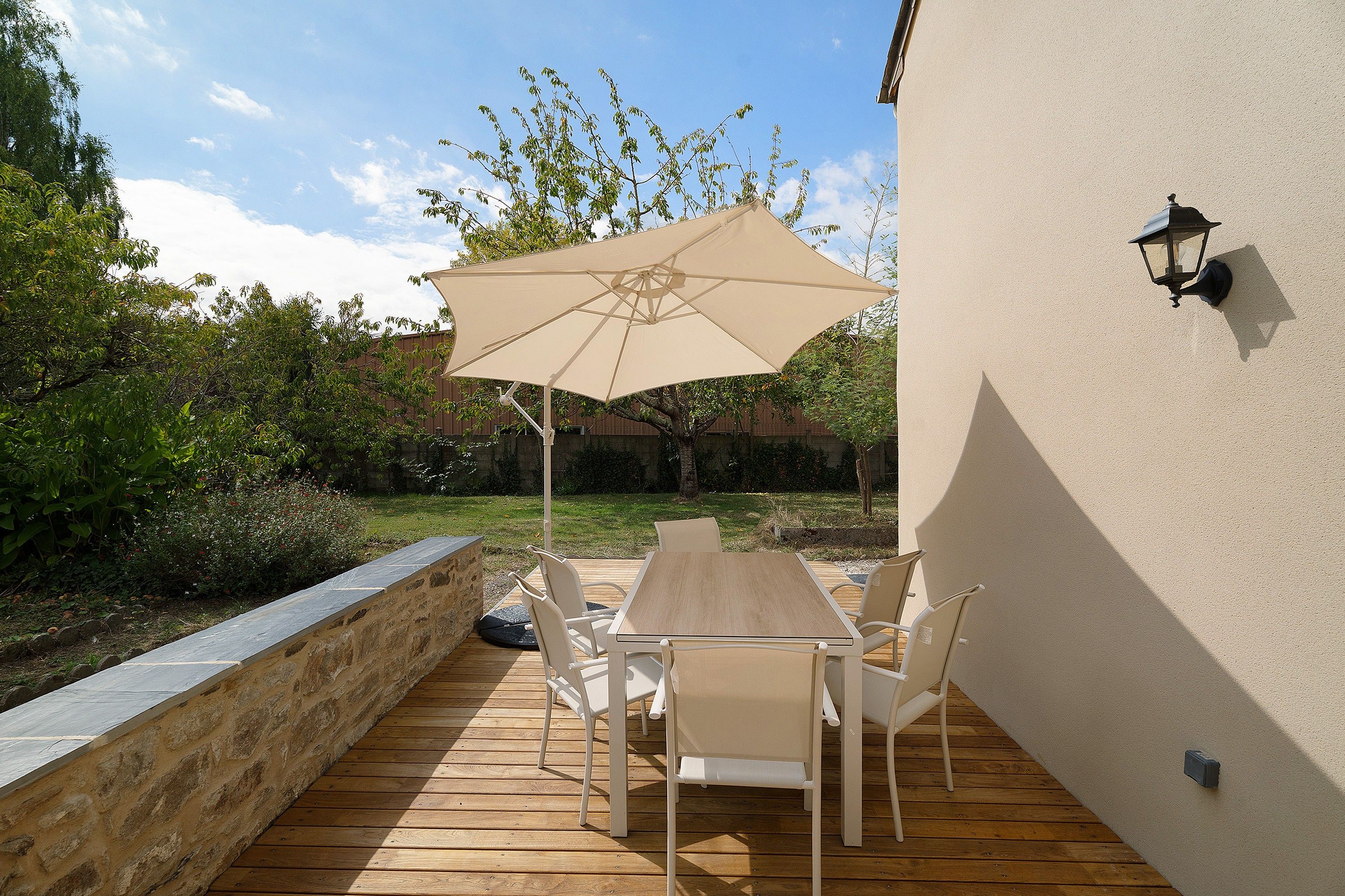 Un patio al aire libre con una mesa, sillas, un paraguas grande y una lámpara fijada a la pared.