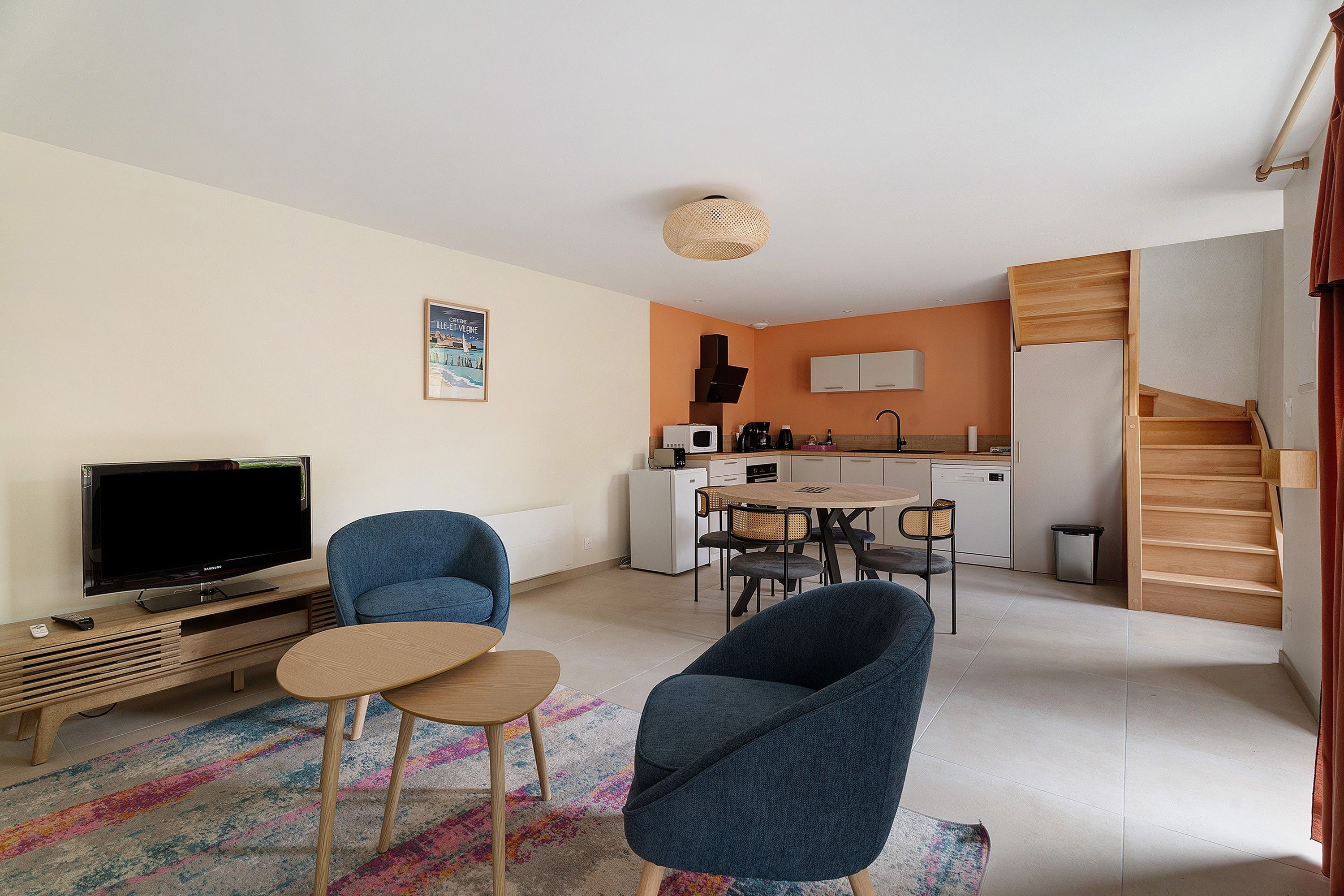 Un espacio habitable compacto con televisor, zona de estar, kitchenette y una escalera.