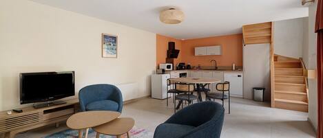 Un espacio habitable compacto con televisor, zona de estar, kitchenette y una escalera.