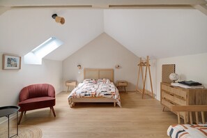 Une chambre avec un plafond en pente, un lit recouvert d’une couvre-lit à motifs, une chaise rouge, une commode en bois et une petite table.