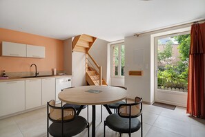 Une cuisine moderne avec une table de salle à manger ronde, deux chaises, un escalier et une vue sur un jardin, visible à travers une grande fenêtre.
