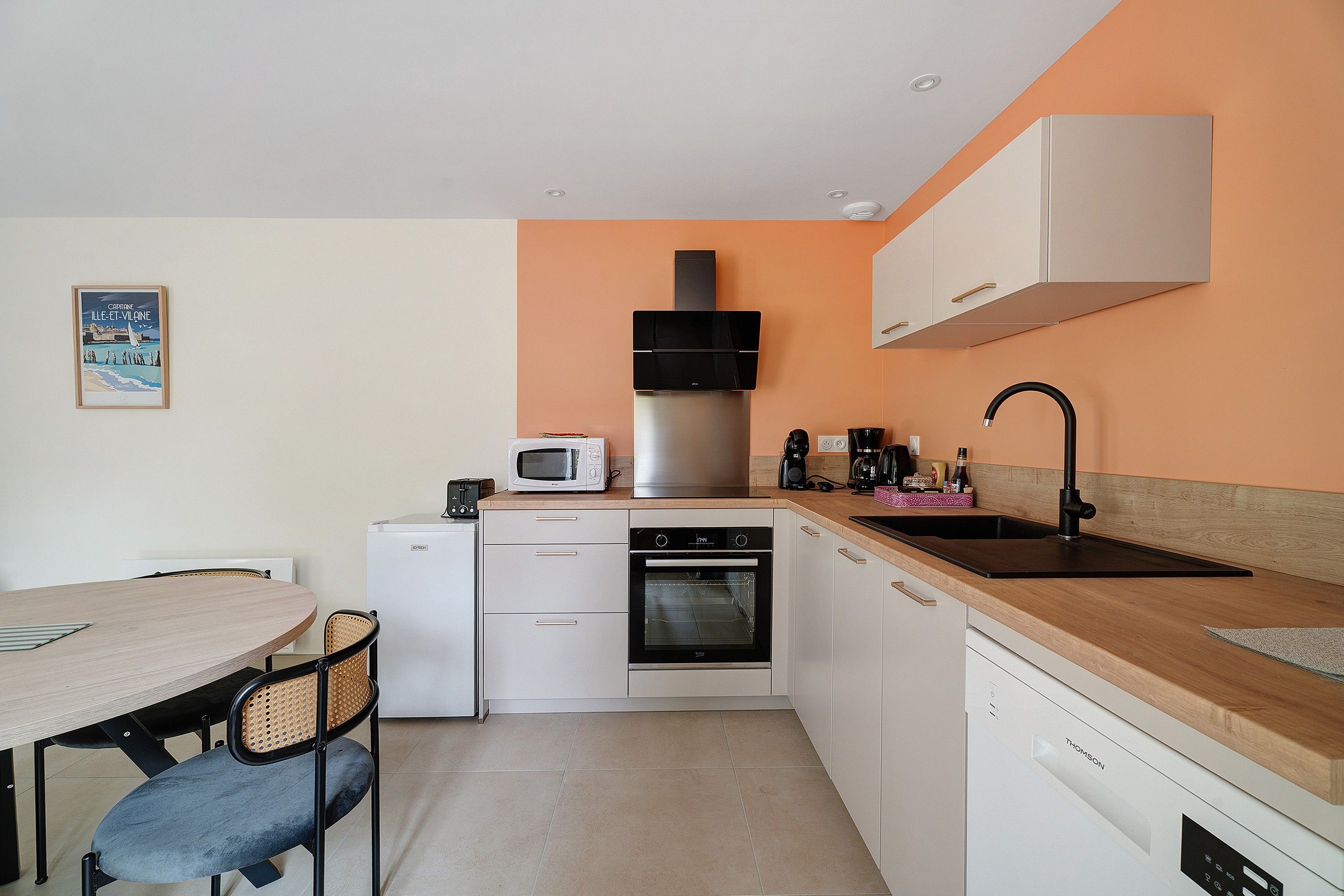 A compact kitchen with a microwave, oven, and sink, featuring white cabinetry and a wooden countertop.