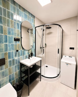 A bathroom with a glass shower enclosure, a sink with a black shelf, and a white toilet. - Kraków Bohaterów Września 6 | AC | Parkside (Kraków)
