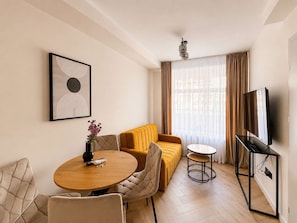 A modern living room with a sofa, a round dining table, a TV, and a painting on the wall. - Kraków Bohaterów Września 6 | AC | Parkside (Kraków)