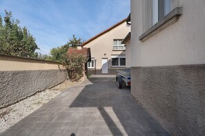 Une ruelle étroite avec un camion garé, un bâtiment doté d’un toit en tuiles et un arbre.