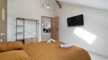 A modern bedroom with a large bed, a wardrobe, a flat-screen TV, and a skylight.