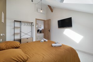 Une chambre moderne avec un grand lit, une armoire, un téléviseur à écran plat et une fenêtre de toit.