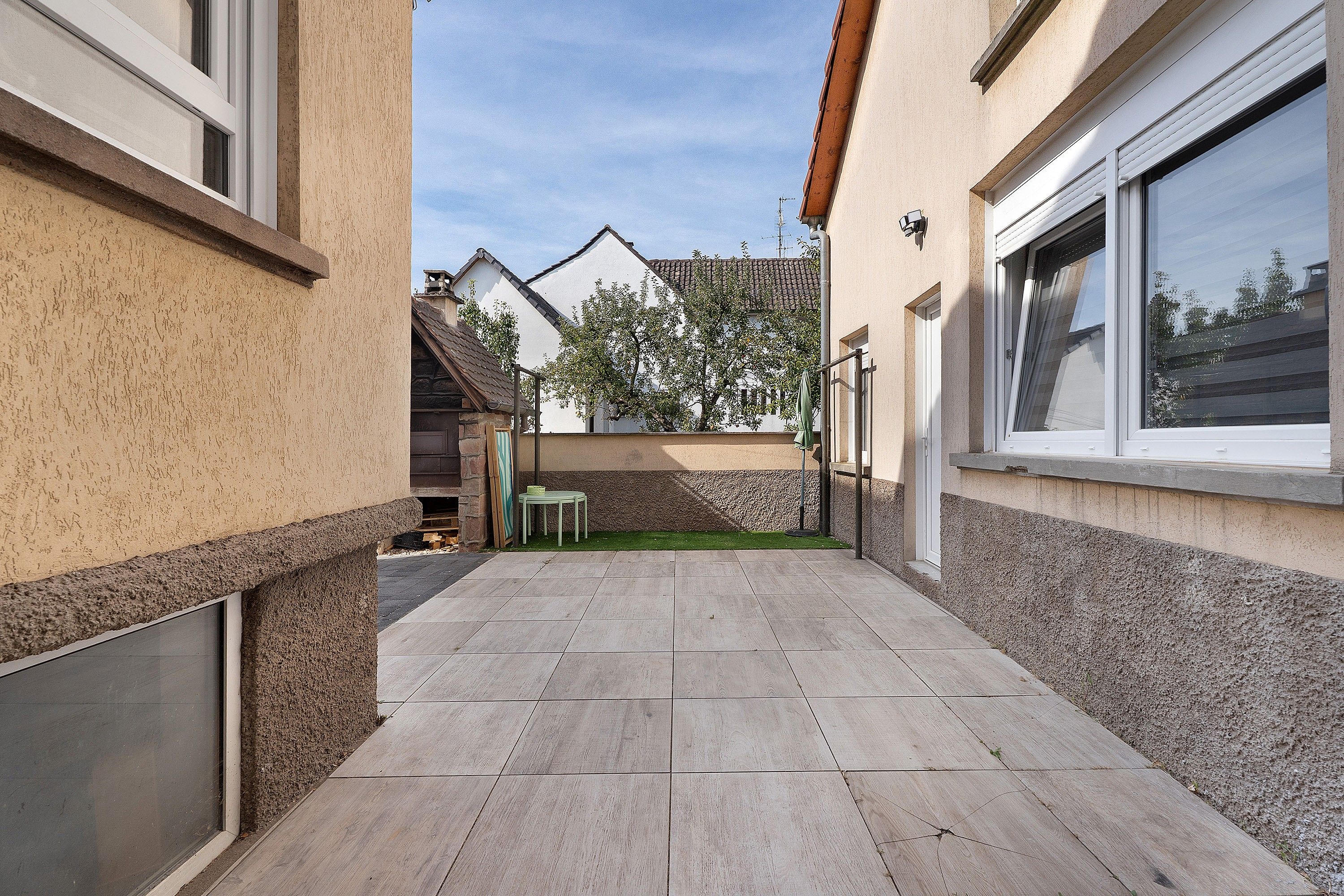 A narrow outdoor corridor with a tiled floor, a small table, and a chair.