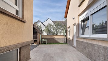 A narrow outdoor corridor with a tiled floor, a small table, and a chair.