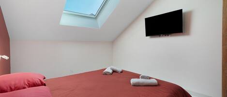 Une chambre avec un lit, un téléviseur à écran plat fixé au mur et une lucarne.