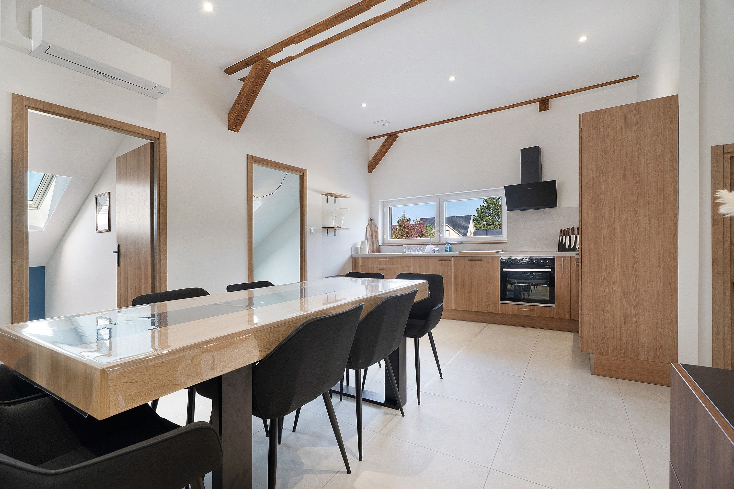 A modern kitchen with a central island, black chairs, and a large window.