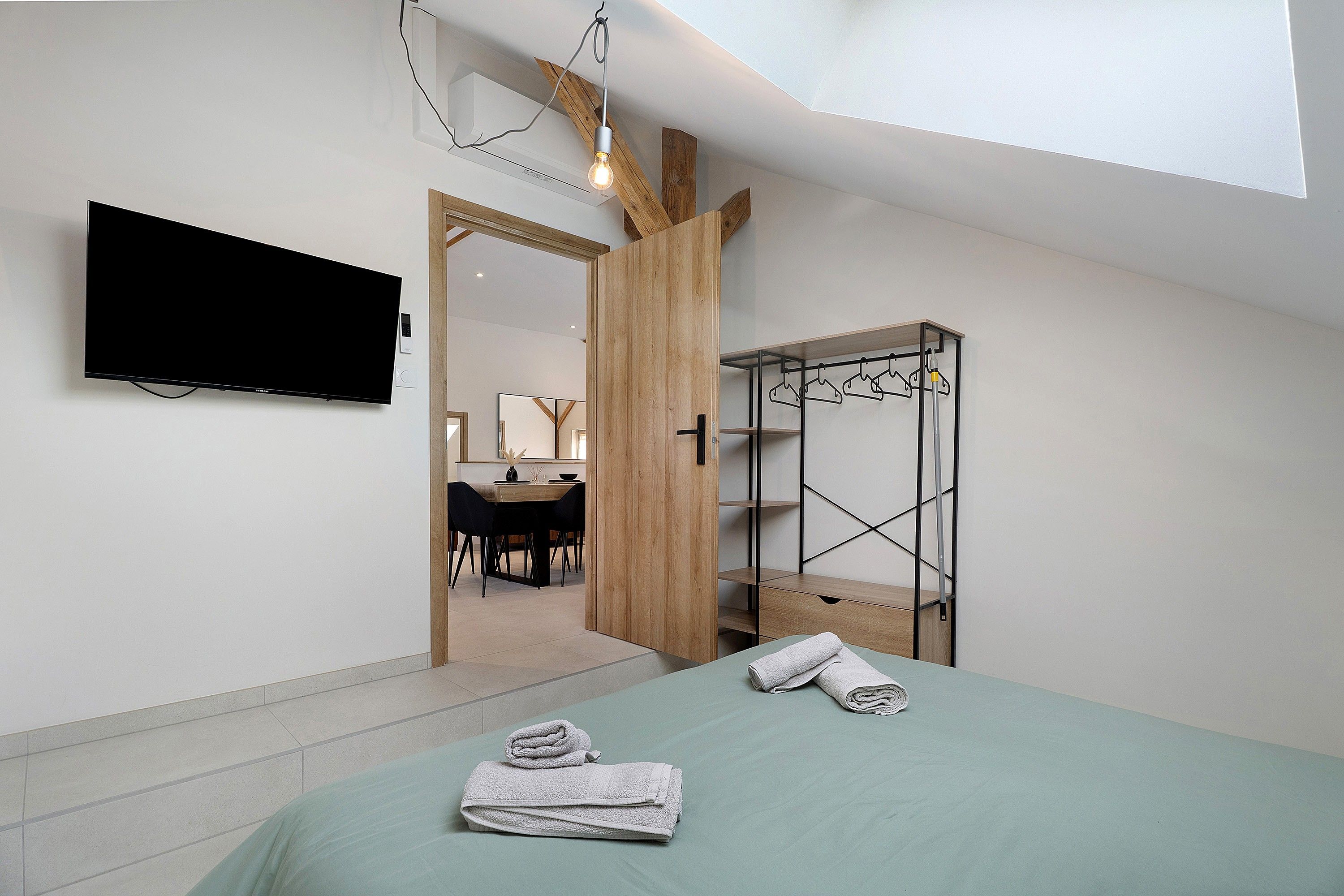 Ein modernes Schlafzimmer mit einem Bett, einem an der Wand montierten Fernseher und einem Holzschrank mit Metallhängersystem.