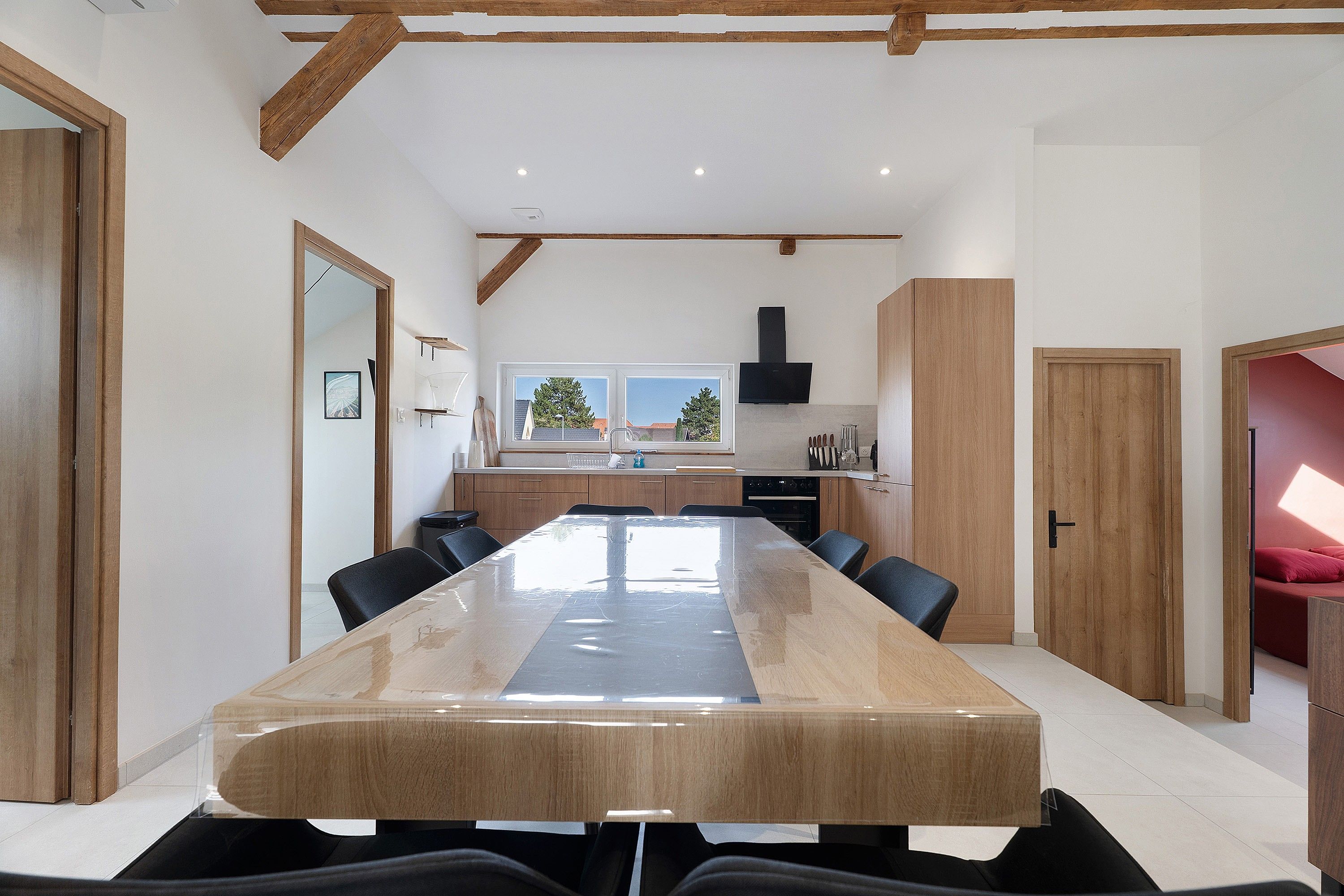 Een ruime eethoek met een lange tafel, houten kasten en een keuken op de achtergrond.