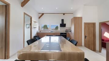 Een ruime eethoek met een lange tafel, houten kasten en een keuken op de achtergrond.