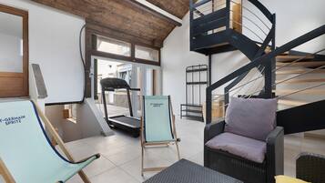 A modern interior with a treadmill, a blue exercise chair, a wicker sofa, and a black spiral staircase.