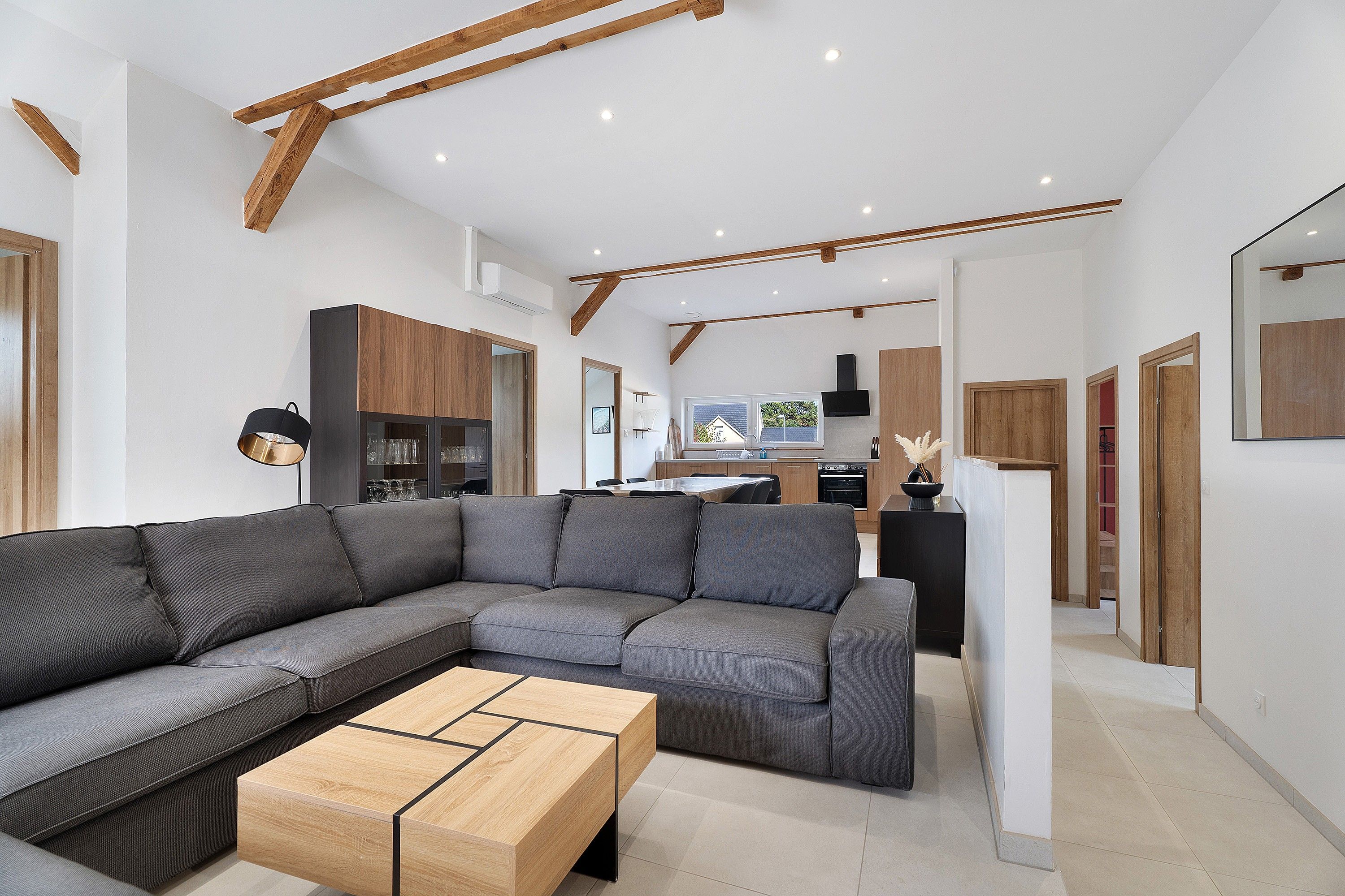 A modern living room with a sectional sofa, a wooden coffee table, and a kitchen in the background.