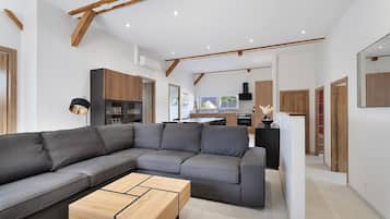 A modern living room with a sectional sofa, a wooden coffee table, and a kitchen in the background.