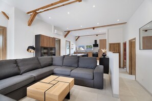 Un salon moderne avec un canapé d’angle, une table basse en bois et une cuisine en arrière-plan.