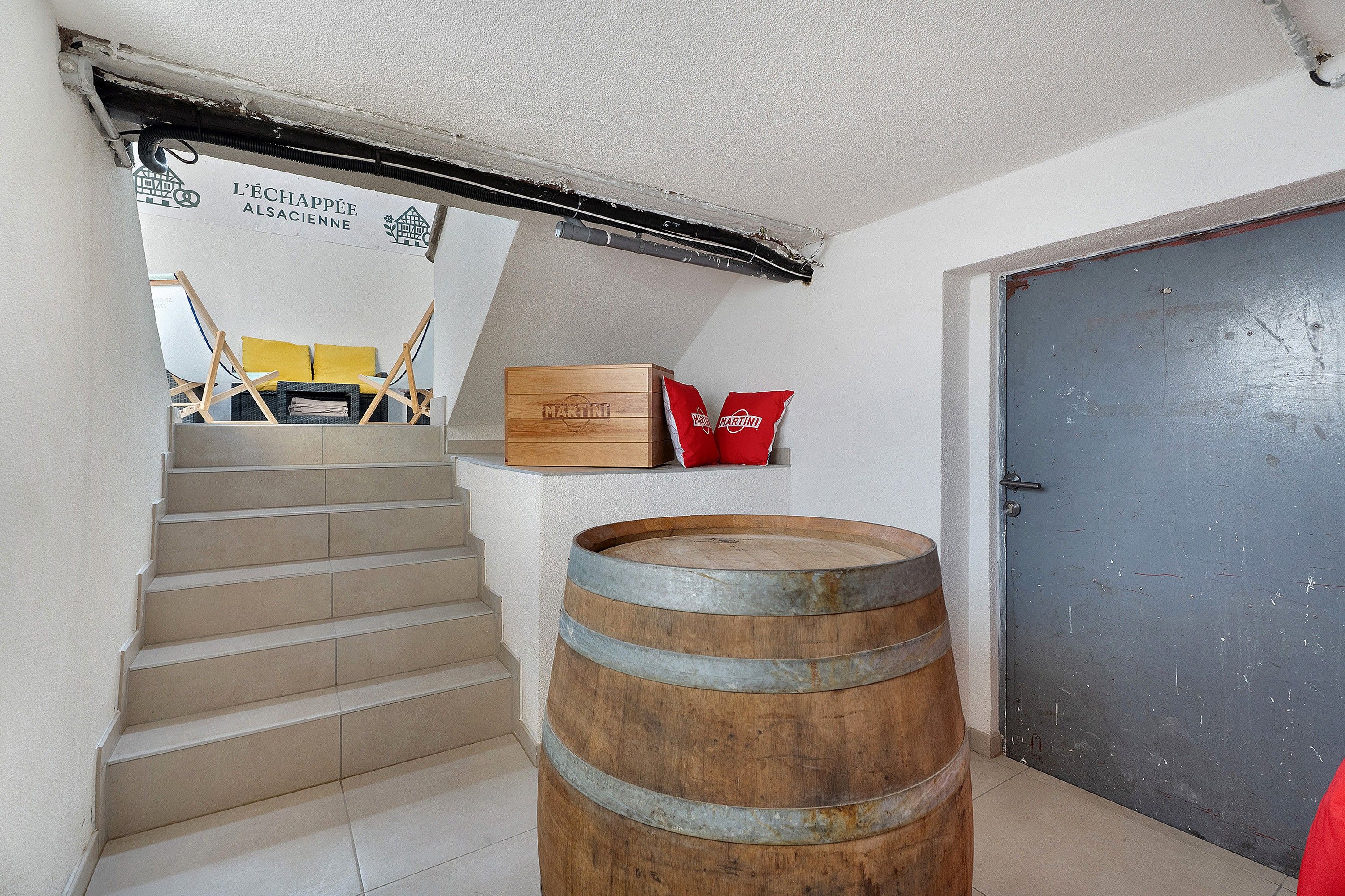Eine Treppe führt zu einer Zwischenebene mit einem Holzfass, einer Tür und einer Wand mit einem Schild.