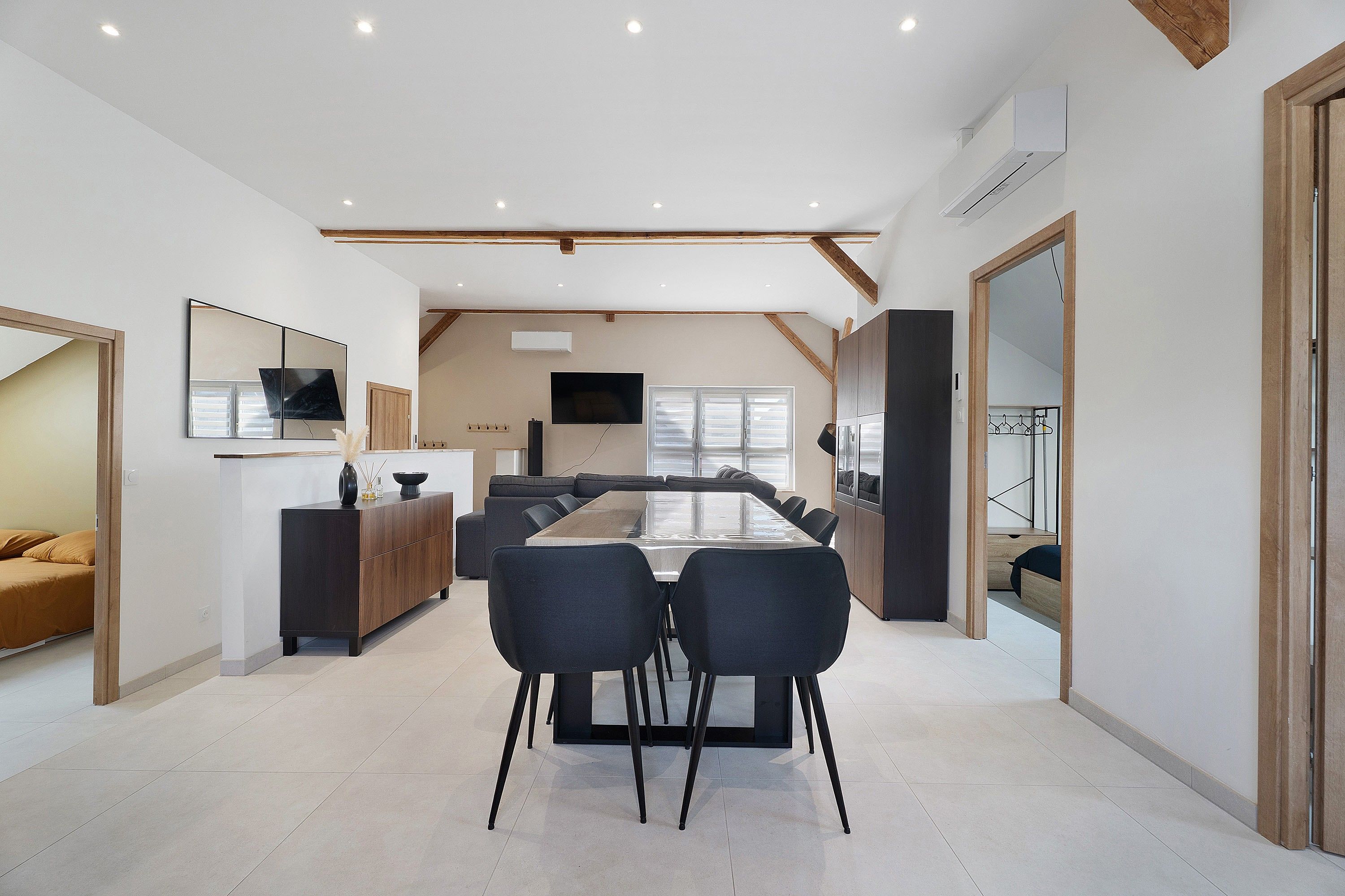 A modern interior with a dining area, sofas, a TV, and a large mirror.