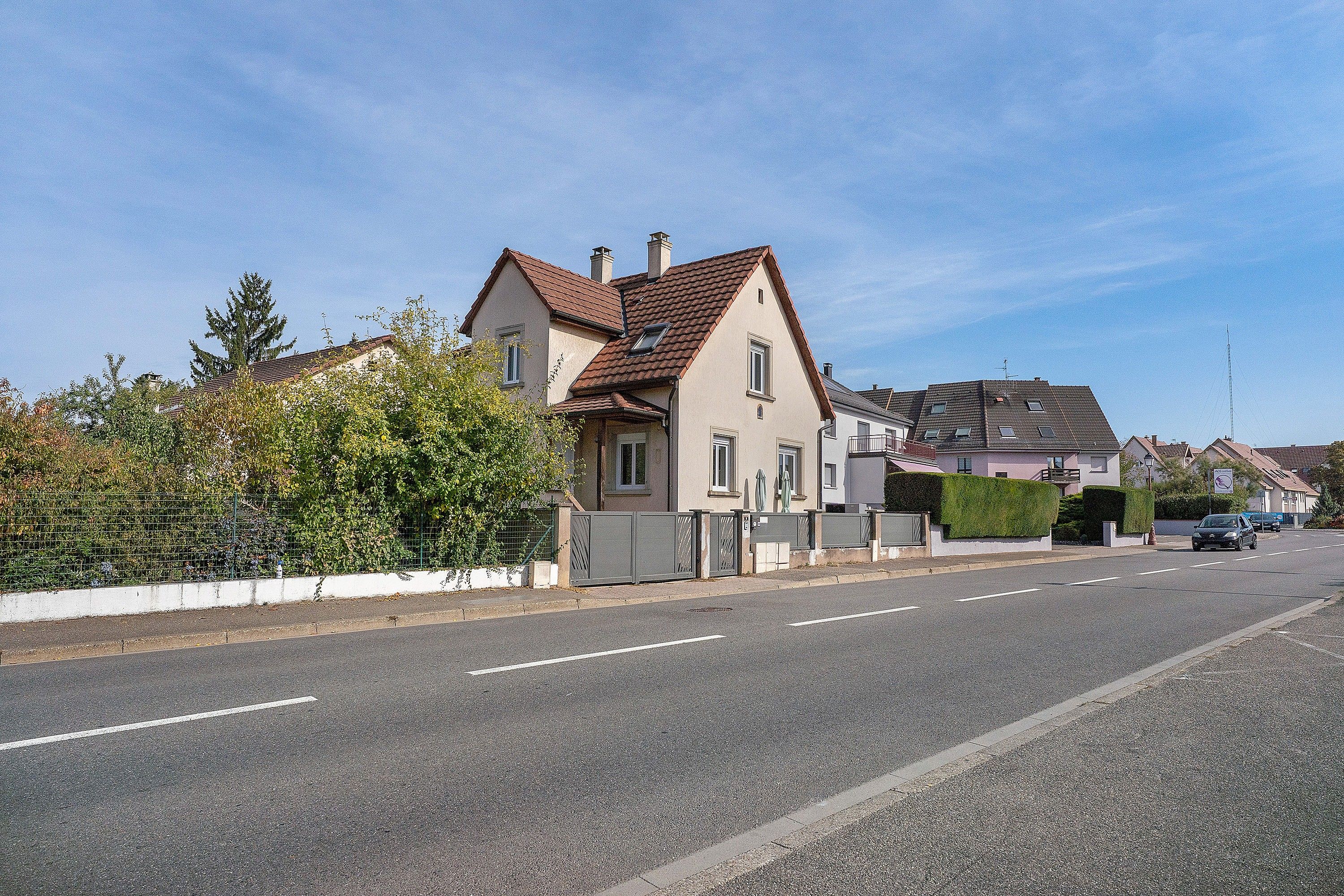 Eine Wohnstraße mit Häusern, blauem Himmel und einem Auto auf der Straße.