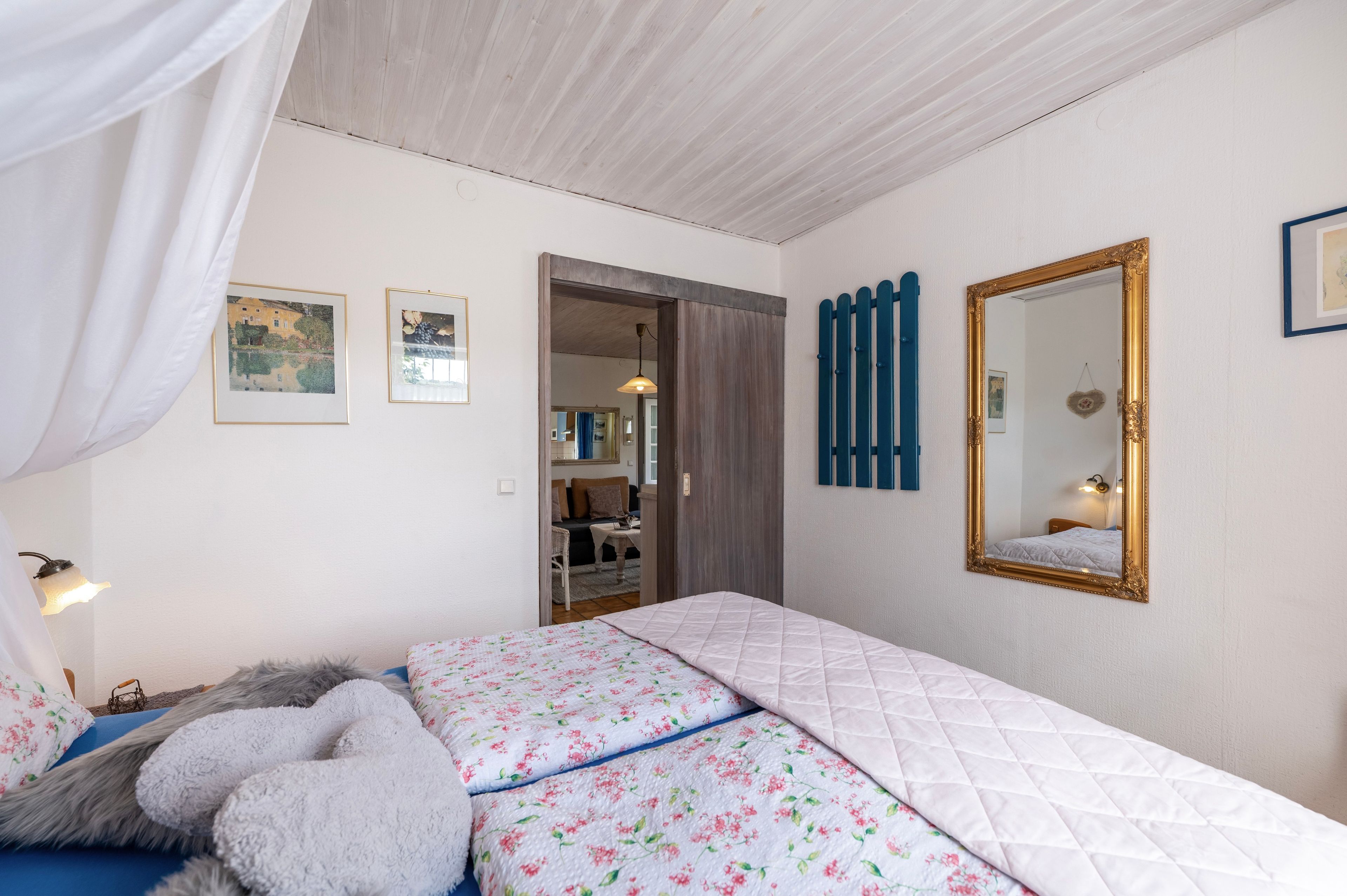 A bedroom with a bed, a mirror, and two framed pictures on the wall.