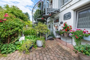 A courtyard with a staircase leading to a balcony, surrounded by lush greenery and potted plants.