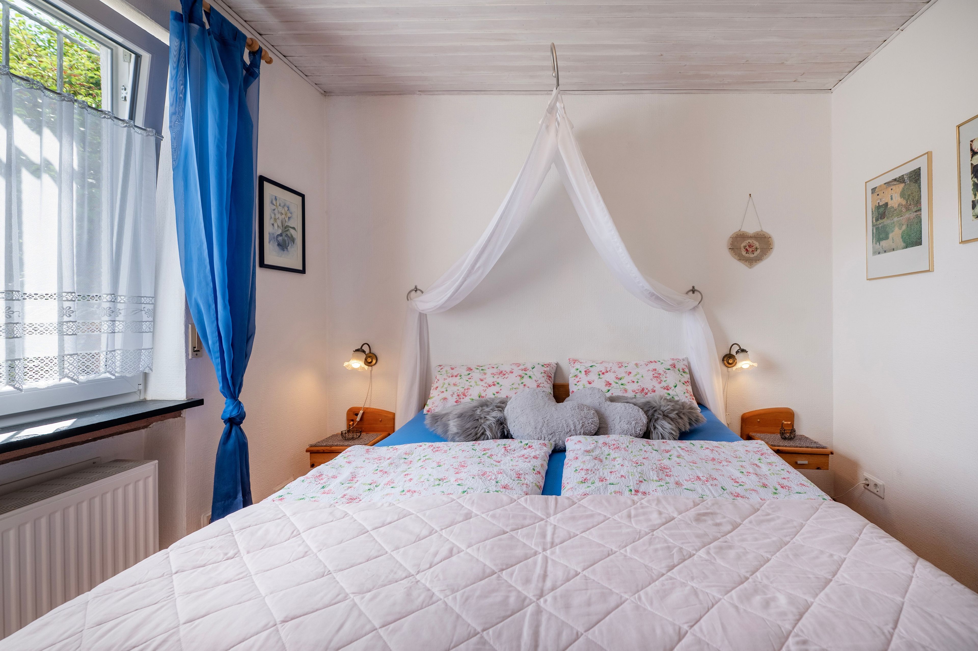 Una camera da letto con un letto, una finestra con tende, lampade sui comodini e quadri alle pareti.