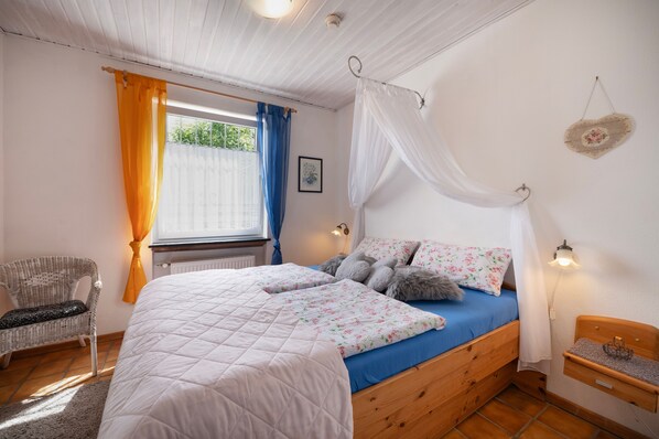 A bedroom with a bed, a chair, a bedside table, and a window with curtains.