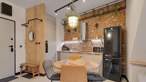 A compact kitchen with a brick wall, a black refrigerator, and a round dining table with chairs. - Granaria D601 | Balcony | AC | TOP Location (Gdańsk)