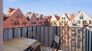 A balcony with a wooden table and chairs, overlooking a row of colorful buildings. - Granaria D601 | Balcony | AC | TOP Location (Gdańsk)