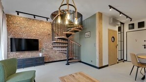 A modern living room with a brick wall, a spiral staircase, a flat-screen TV, and a dining area with a round table and chairs. - Granaria D601 | Balcony | AC | TOP Location (Gdańsk)