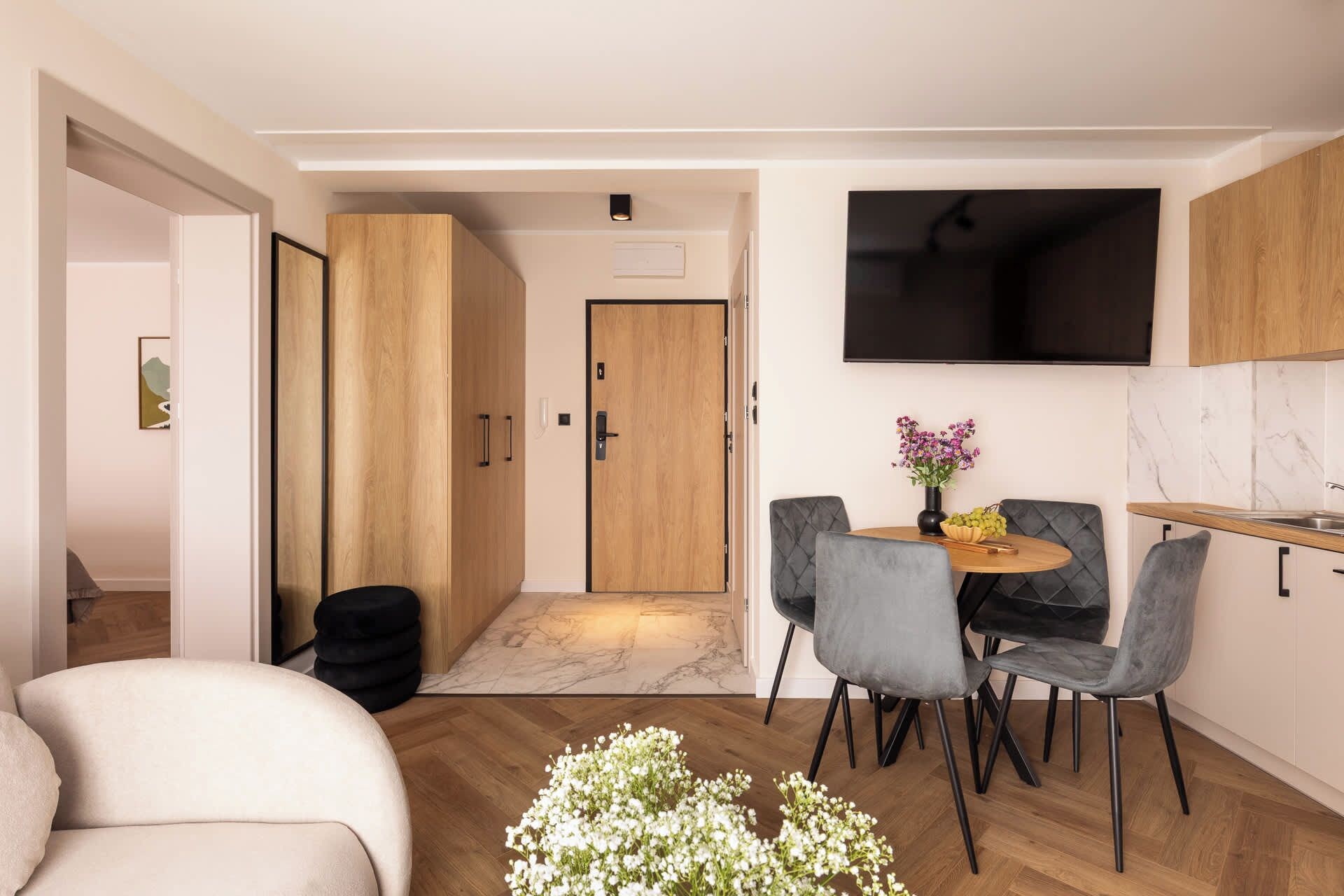 Ein kompakter Wohnbereich mit Essplatz, einem an der Wand befestigten Fernseher und einer Holztür.