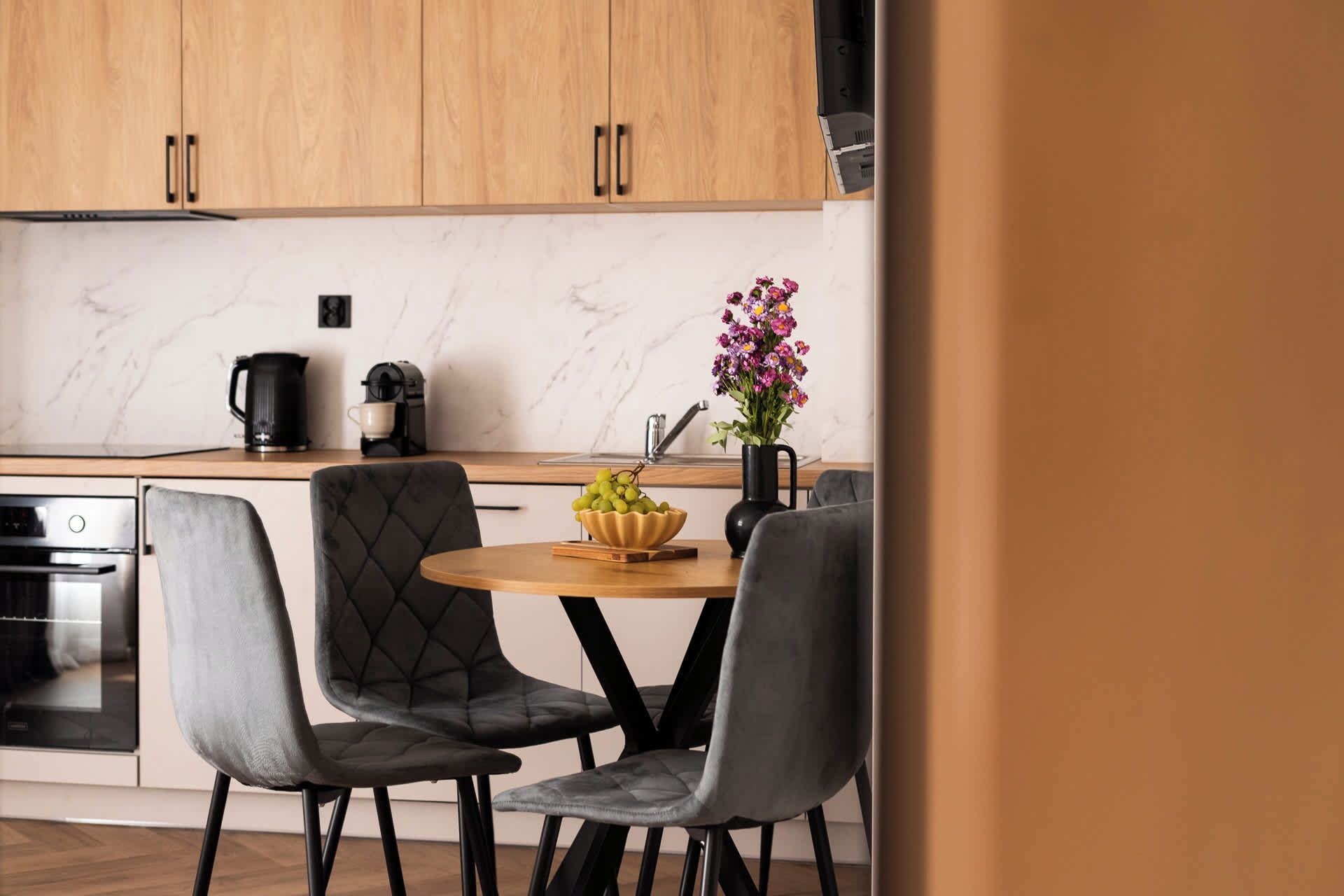 Eine moderne Küche mit Holzschränken, einer Marmorarbeitsplatte, einer Kaffeemaschine, einer Vase mit Blumen und zwei Polsterstühlen.