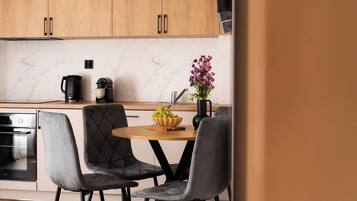 A modern kitchen with wooden cabinets, a marble countertop, a coffee maker, a vase with flowers, and two upholstered chairs.