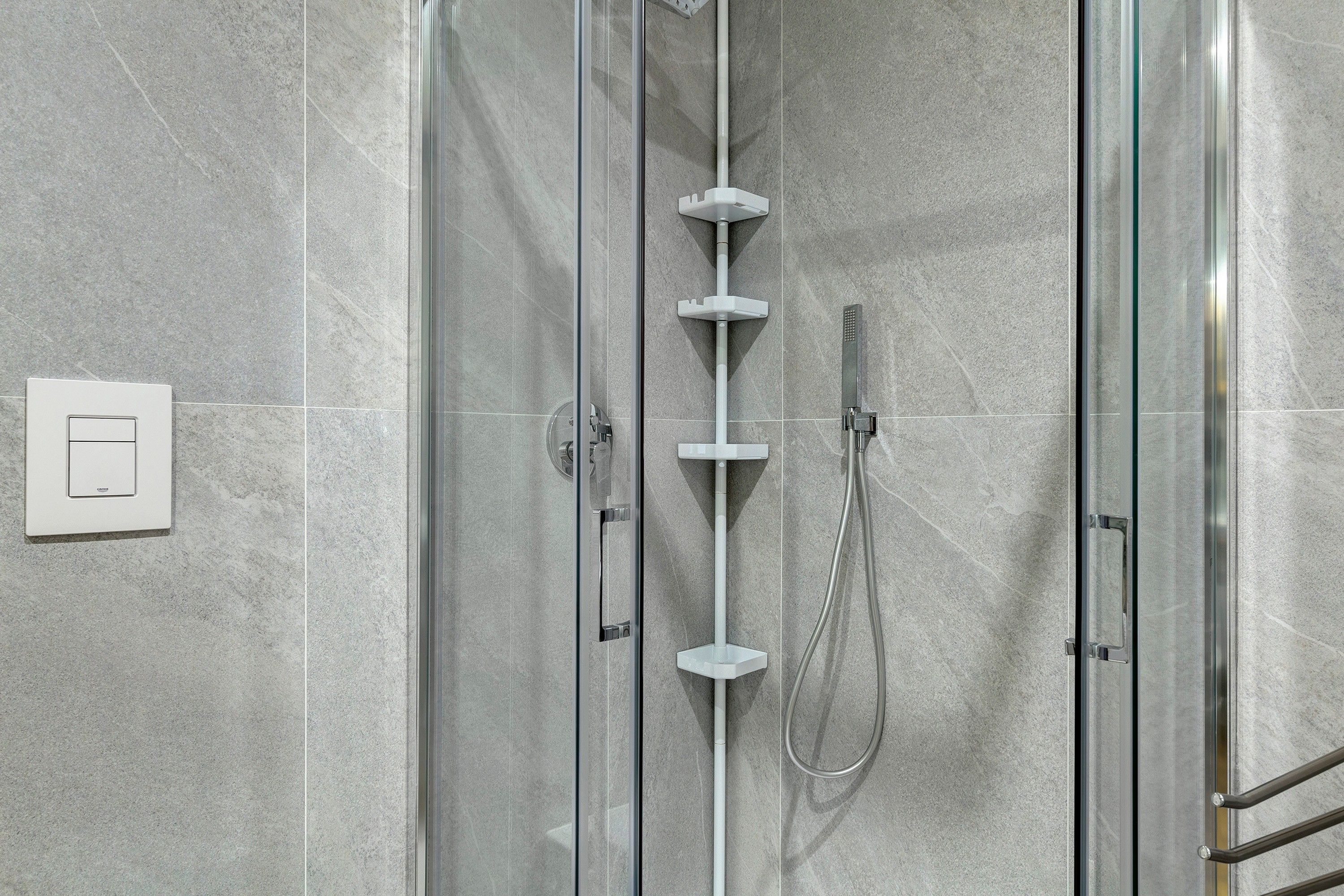 Une douche fermée par des parois en verre, dotée d’un pommeau de douche à main et d’un flexible de douche à main.