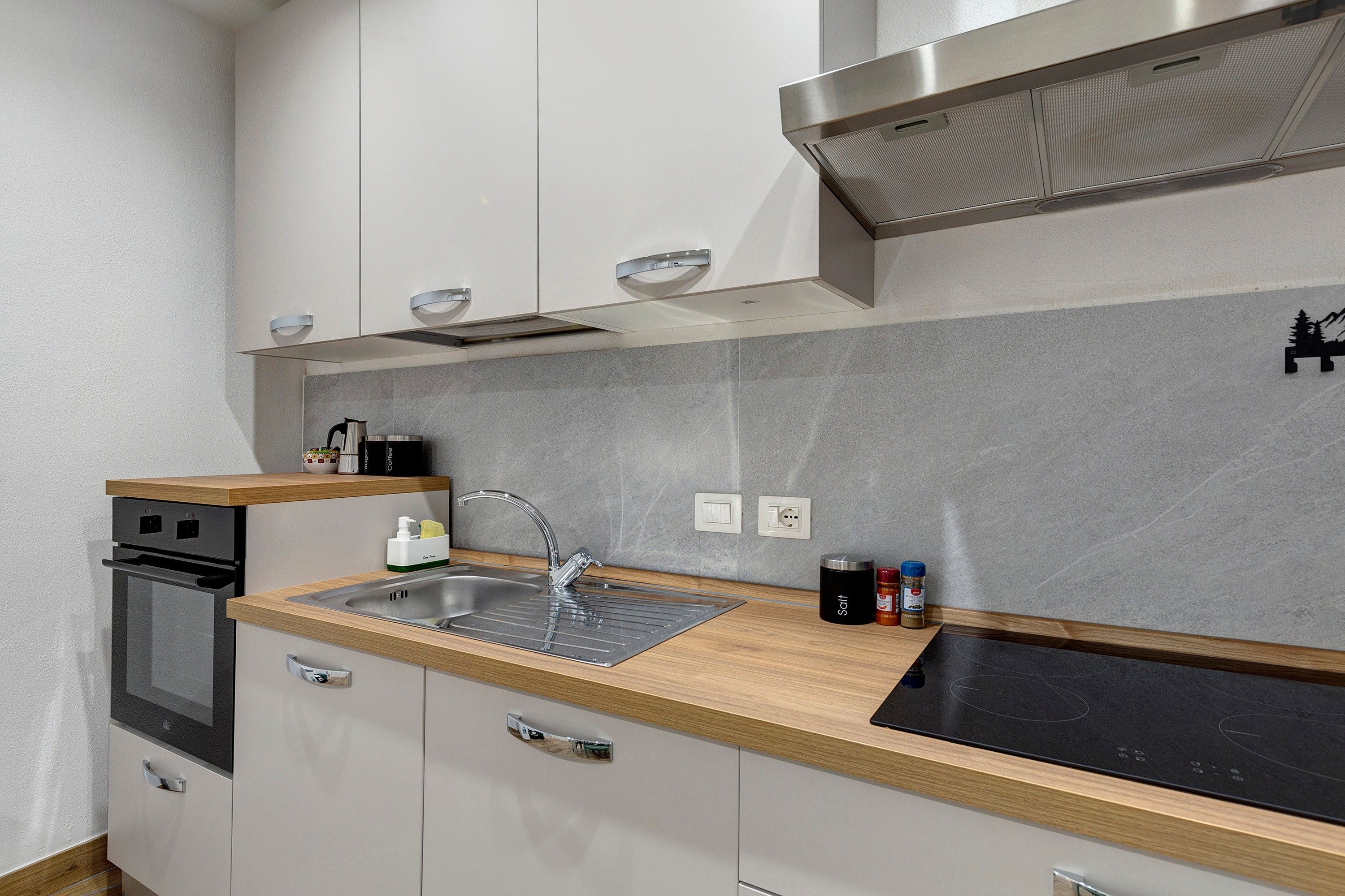 A modern kitchen with a stainless steel sink, a built-in oven, and a range hood.