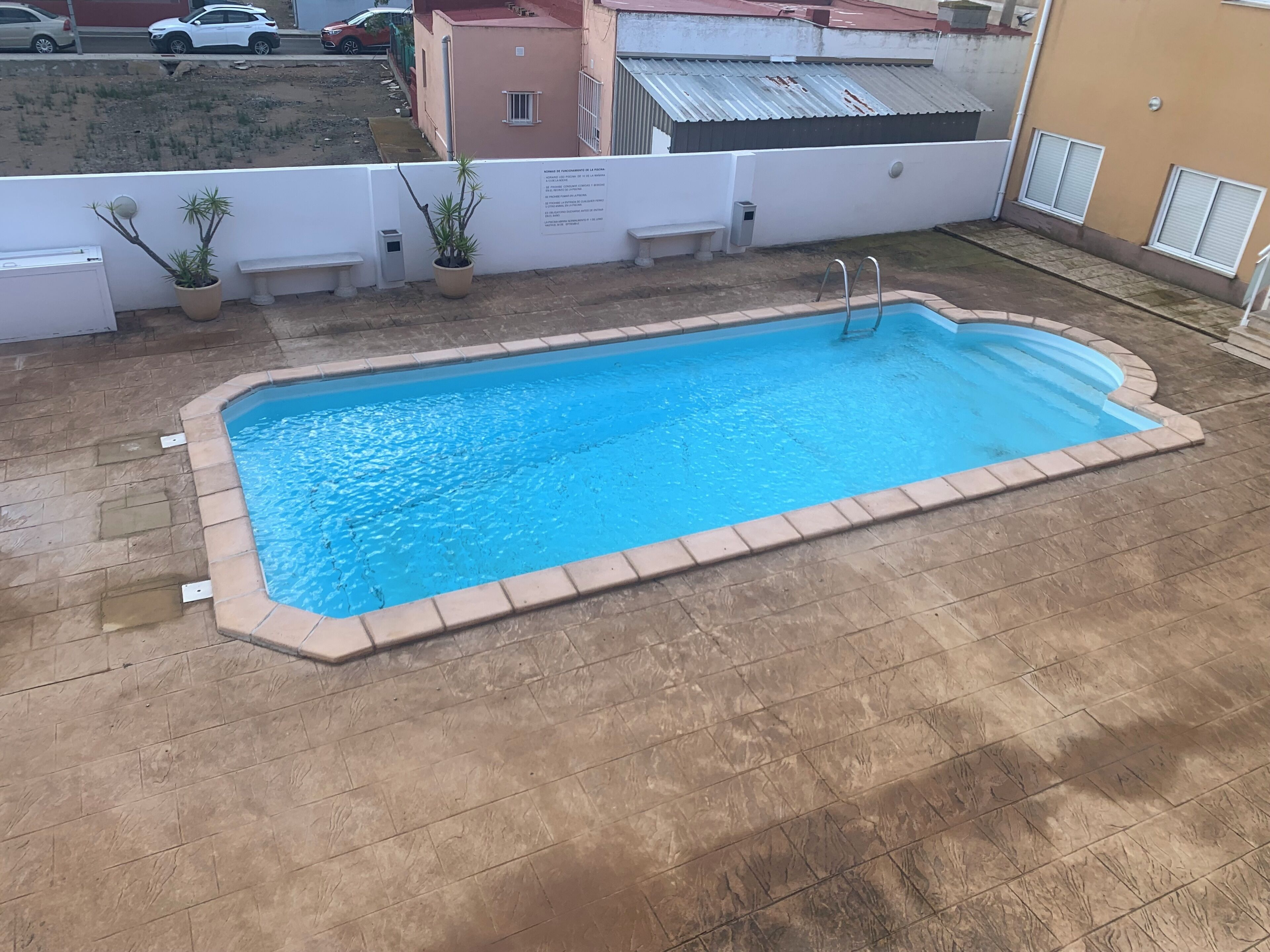 A rectangular outdoor swimming pool with a tiled edge, surrounded by a brick patio.