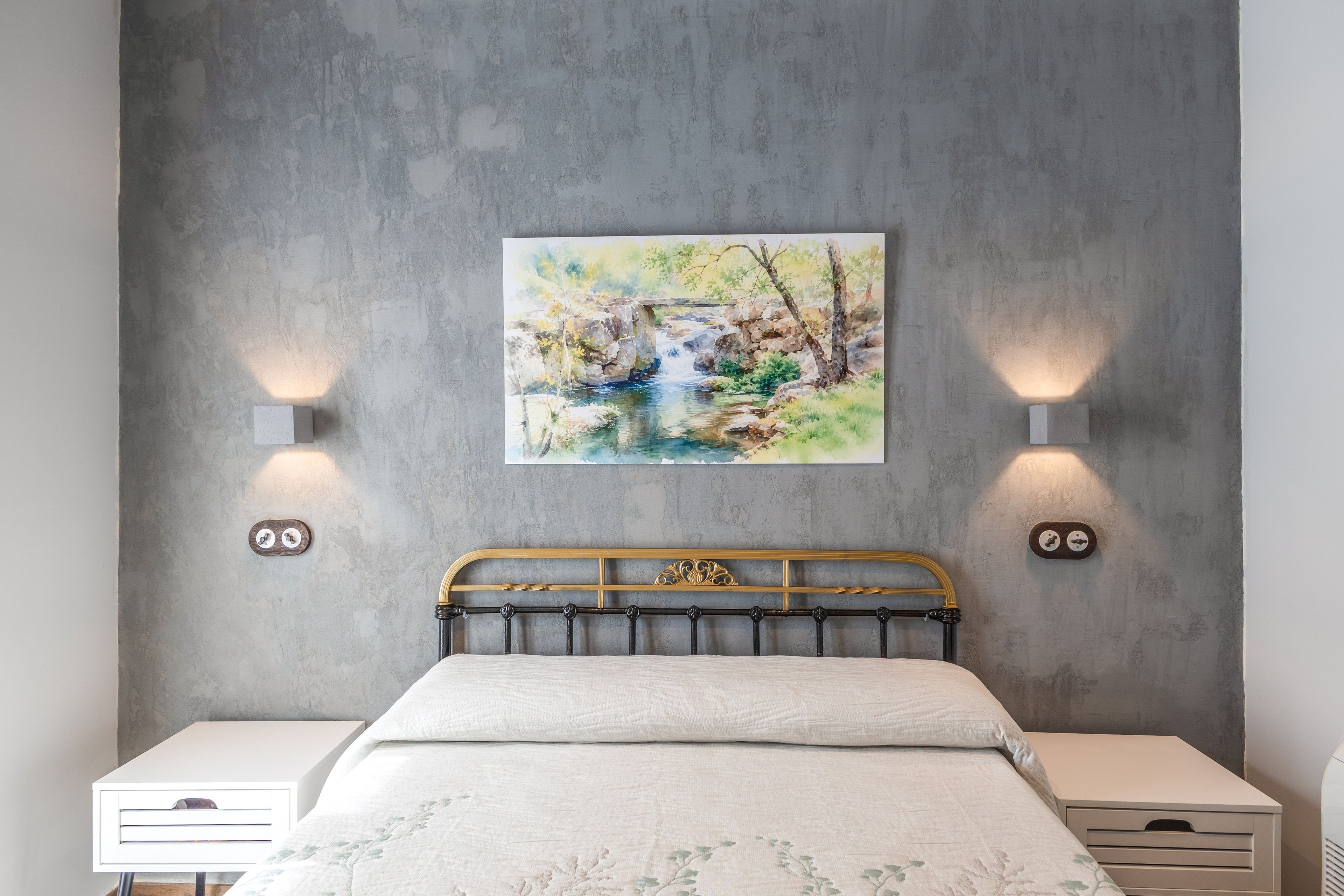 Une chambre à coucher comprenant un lit, deux tables de chevet, un tableau accroché au mur et deux appliques murales.