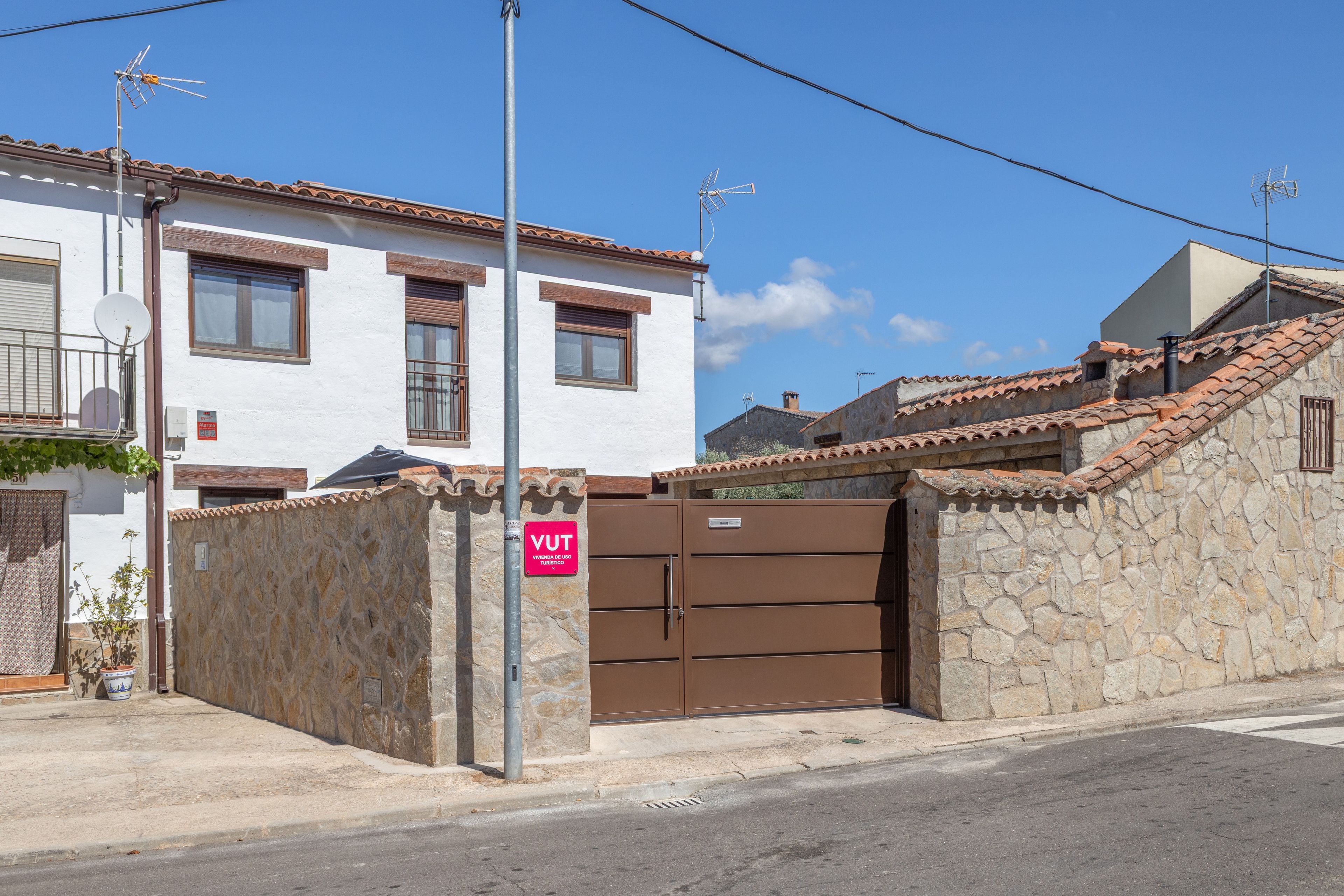 A residential building with a stone wall, a gated entrance, and a clear sky.